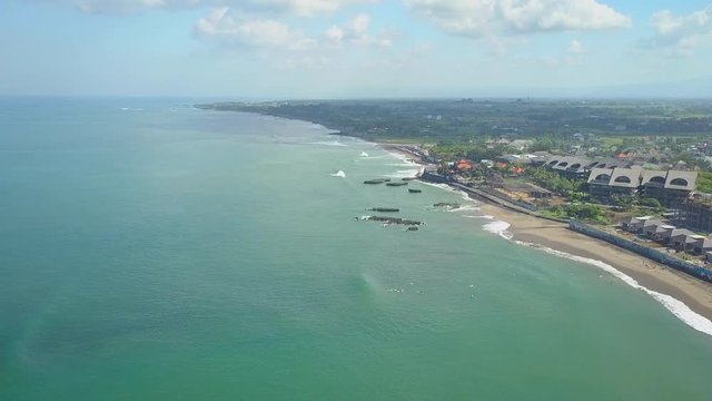 AERIAL: Flying above crowds of surfers catching turbulent foamy waves at Canggu beach Bali surfspot. Surfboarders riding the sea. Scenic luxury tourist resort & beautiful sunny tropical island scenery