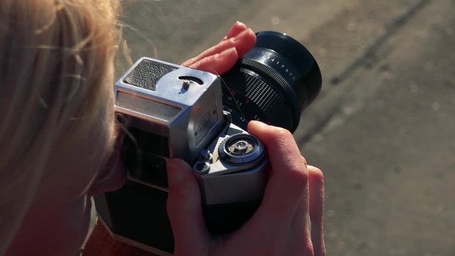 A blonde woman takes photos with a camera in a street - closeup from above