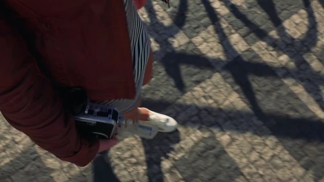 A woman holds a video camera and walks down a street - closeup from above on the hand