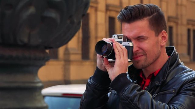 A young handsome man takes photos of a statue with a camera - closeup - a busy street in the blurry background