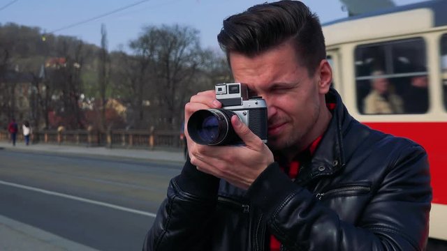 A young handsome man takes photos with a camera - closeup - a busy road in the blurry background