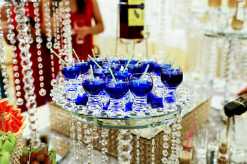 Glasses with blue drinks stand on mirror tray decorated with crystal chains hanging from it