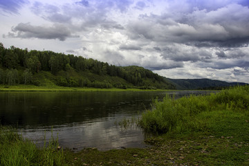 landscape with river, mountains and forest on a shore. Sky with storm clouds over the river