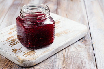 Raspberry jam in a glass jar on wooden table. Space for text