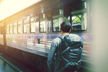 Behind asian young man standing and waiting train on platform.