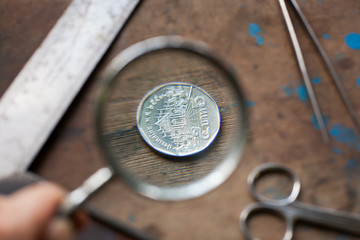 Close up coin and magnifying glass on wood background selective and soft focus hipster tone