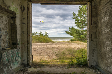 Coastal landscape with dune, Baltic Sea and pine trees seeing through a frame of old destroyed building
