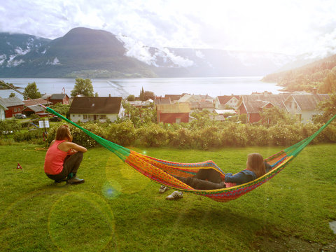 junge Frauen genießen ihre Auszeit in einer Hängematte und auf der Wiese mit Blick auf einen Fjord - Solvorn, Norwegen