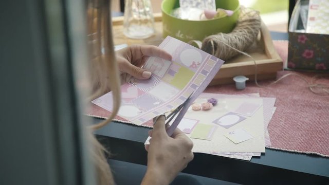 Accessories for scrapbooking on the desktop. Homemade greeting is open: fittings for needlework and the process of creation. Process of cutting out paper from parts and elements for postcards. Hobby.
