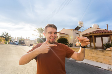 Young man holding house keys on house shaped keychain in front of a new home.