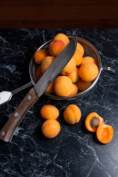 Fresh organic apricots in steel colander. Group of harvested apricots whole and halved in steel colander and vintage knife..