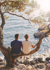 romantic young couple in love together. Happy young couple in love sitting and kissing on a tree branch on sea in background