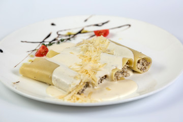 Delicious meat filled pasta on a plate on white background. Italian cannelloni, Spanish canelones.