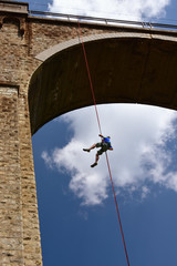 Young man descending by rope from a high stone-built railroad bridge in a sunny summer day © Didi Lavchieva