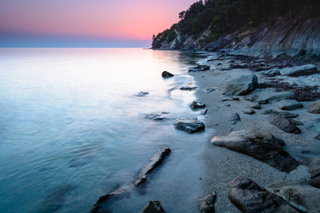 Long exposure of a dreamy and colorful sunset on a rocky beach in Chalkidiki, Greece