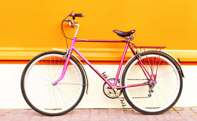 Retro old pink bicycle stands on a colorful orange background