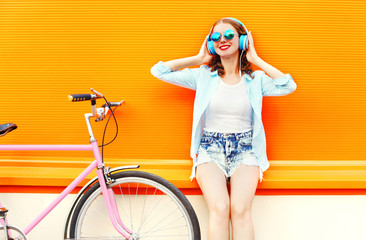 Summer fashion woman listens to music in headphones near retro pink bicycle