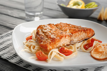 Plate with pasta, salmon, cherry tomatoes and sliced lemon on wooden table