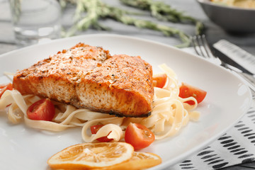 Plate with pasta, salmon, cherry tomatoes and sliced lemon, closeup