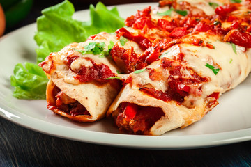 Traditional mexican enchiladas with chicken meat, spicy tomato sauce and cheese on a plate