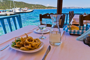 Fried squid and white wine in a shade of a typical greek taverna in a harbour at Amoulani island,...
