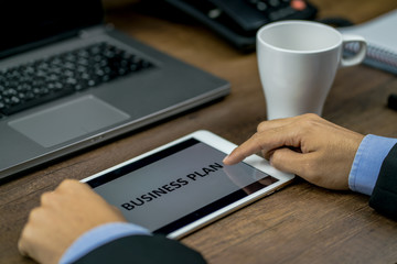 Fototapeta na wymiar Close-up photo of Businessman's hands reviewing or checking the business plan by using digital tablet on the wood desk with laptop and phone in background
