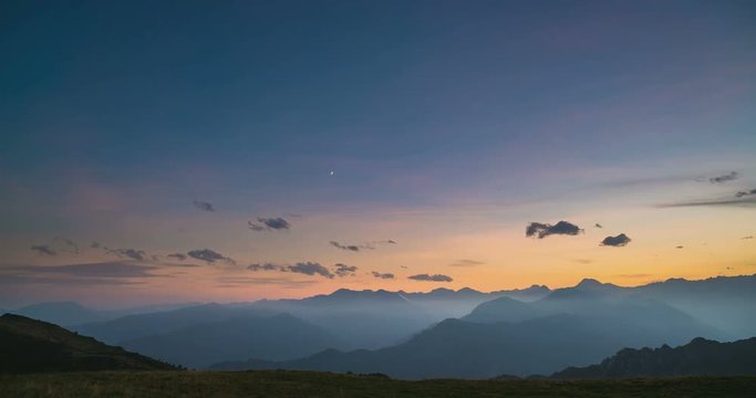 Day to night time lapse from high up on the Alps. Colorful sunset over mountain peaks and fog in the valleys below, moving clouds, setting moon, rotating stars and Milky Way. Static version.