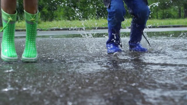 PAN with low section of children in rubber boots jumping in puddle and splashing water during rain