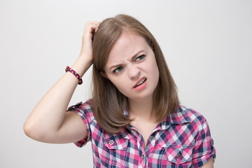 Fototapeta premium Caucasian girl scratching her head, thinking of something, looks bewildered