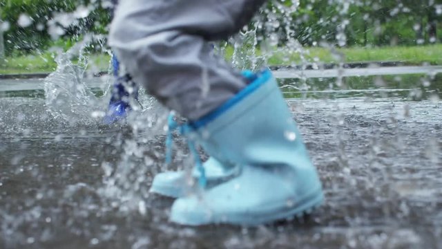 Low section with slow motion of legs of children in rubber boots jumping in puddle during rain