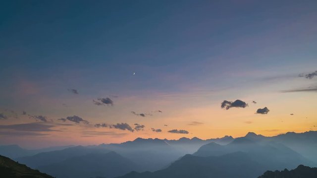 Day to night time lapse from high up on the Alps. Colorful sunset over mountain peaks and fog in the valleys below, moving clouds, setting moon, rotating stars and Milky Way. Sliding version.