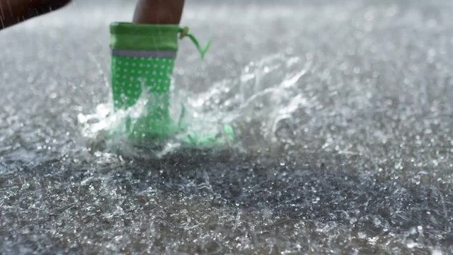 Tracking with low section of legs of children wearing colorful rubber boots walking through puddle during heavy rain
