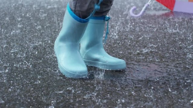 Low section with slow motion of legs of child in blue rubber boots stomping in puddle