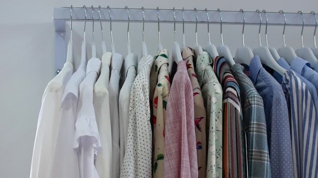 The shirts hang on the hangers in the store. Choose clothes at home or in the store.