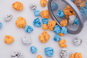 Colorful crumpled paper balls rolling out of a trash can