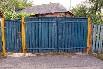 сельский синий деревянный забор и закрытые двери на улице у дороги 