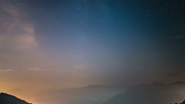 Time Lapse of the Milky way and the starry sky moving over the Italian Alps with fog and moisture resulting in a dreamlike effect. Glowing valleys below. Sliding version.