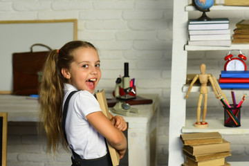 Schoolgirl holds book on light brick wall classroom background