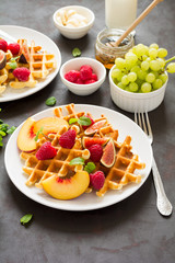 Homemade Belgian waffles with peach, raspberry, fig and honey on brown wooden background. Selective focus