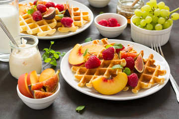 Homemade Belgian waffles with peach, raspberry, fig and honey on brown wooden background. Selective focus