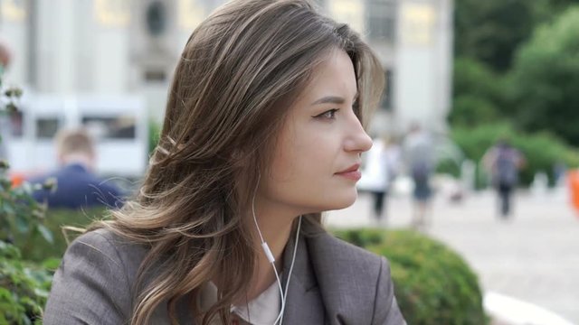 Attractive businesswoman relaxing in the city and listening music on earphones, steadycam shot

