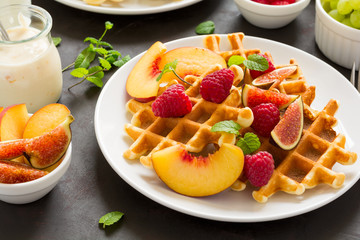 Homemade Belgian waffles with peach, raspberry, fig and honey on brown wooden background. Selective focus