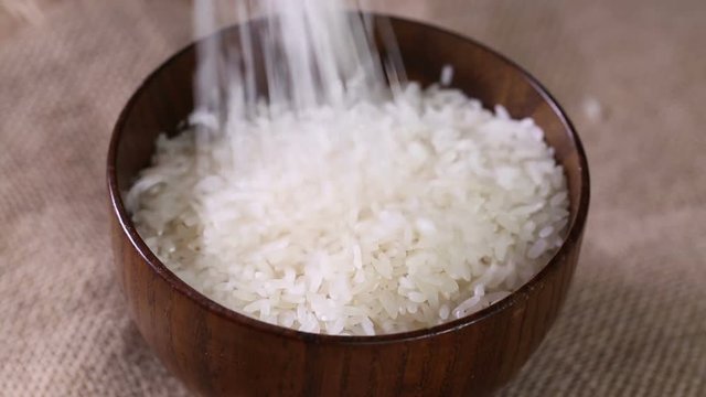 Rice falling to a wooden bowl.