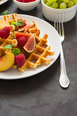 Homemade Belgian waffles with peach, raspberry, fig and honey on brown wooden background. Selective focus