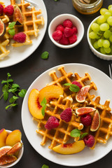 Homemade Belgian waffles with peach, raspberry, fig and honey on brown wooden background. Selective focus