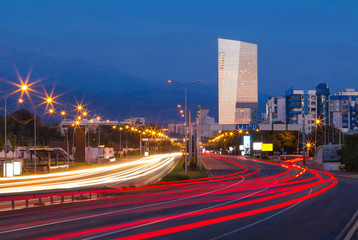 Fototapeta premium Traffic on a freeway. An urban highway early in the morning. Blurry traffic light trails over the road. Distant buildings and mountains are in the background.