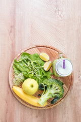 Fresh green vegetables and green smoothie in jar. Detox, diet or healthy food concept. Mason jar of dietary drink with broccoli, spinach, microgreens, lime and banana on wooden background. Top view.