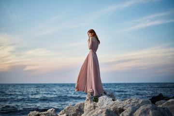 A woman in a long dress is standing on stones near the sea