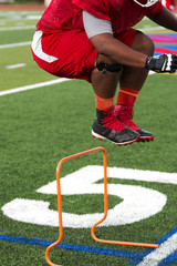 Lineman jumping over orange hurdles at football practice