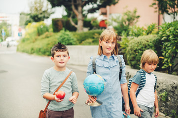 Fototapeta na wymiar Group of three funny kids wearing backpacks walking back to school. Girl and boys enjoying school activities. Globe, lunch box, red apple and bag accessories.